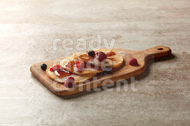 Three stacked mixed berries pancakes on a wooden board on beige background