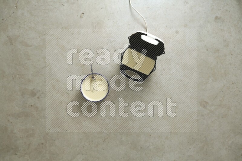 A ceramic bowl beside a carton of eggs and glass bowl full of sugar, vanilla extract, flour on beige marble background