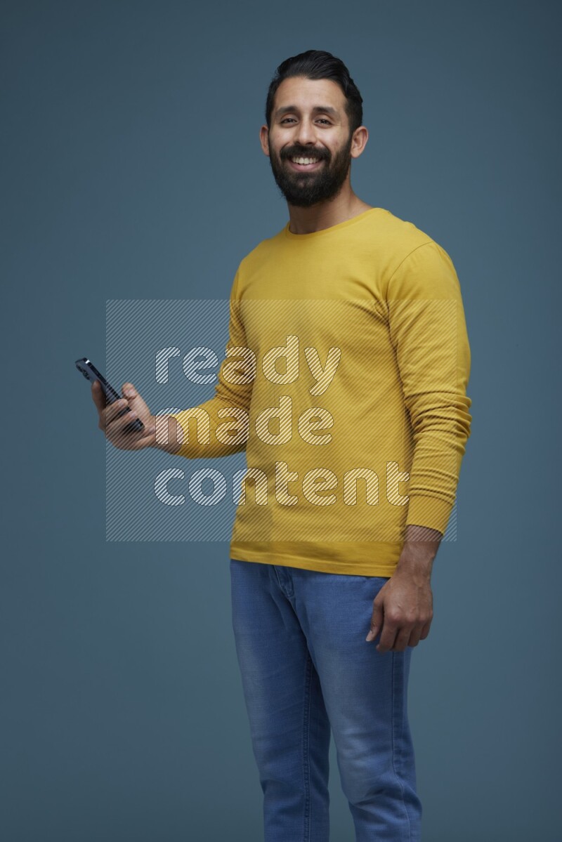 Man posing with a phone in a blue background wearing a yellow shirt
