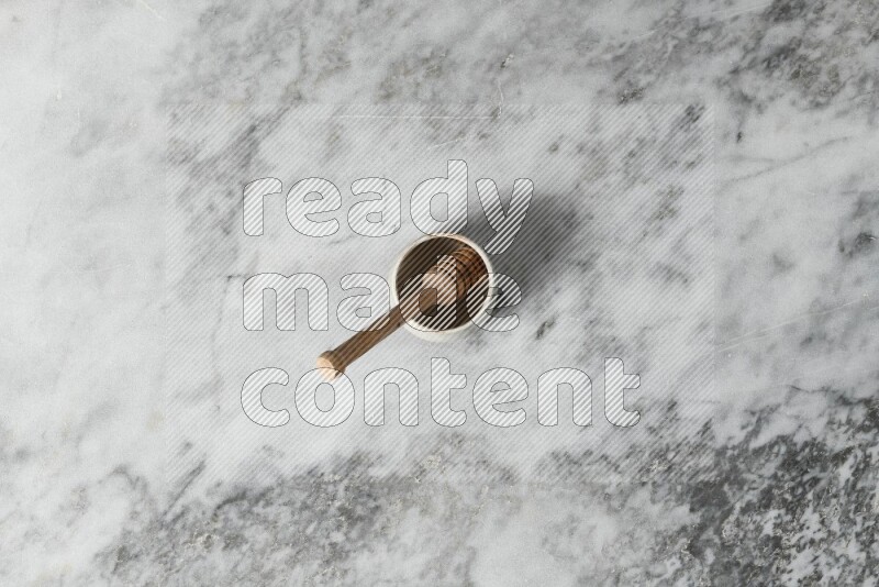 Beige pottery bowl with wooden honey dipper in it on grey marble background
