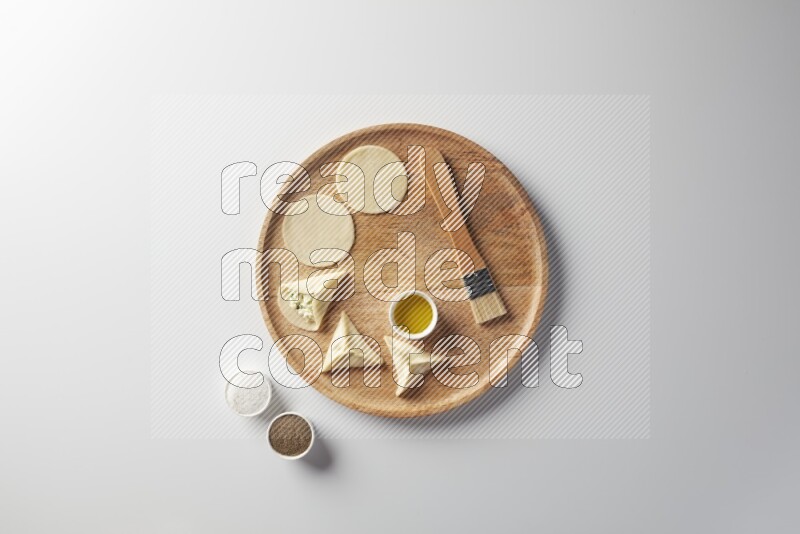 two closed sambosas and one open sambosa filled with cheese while salt, black pepper and oil with oil brush aside in a wooden dish on a white background