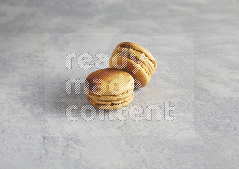 45º Shot of two Yellow Crème Brulée macarons on white  marble background