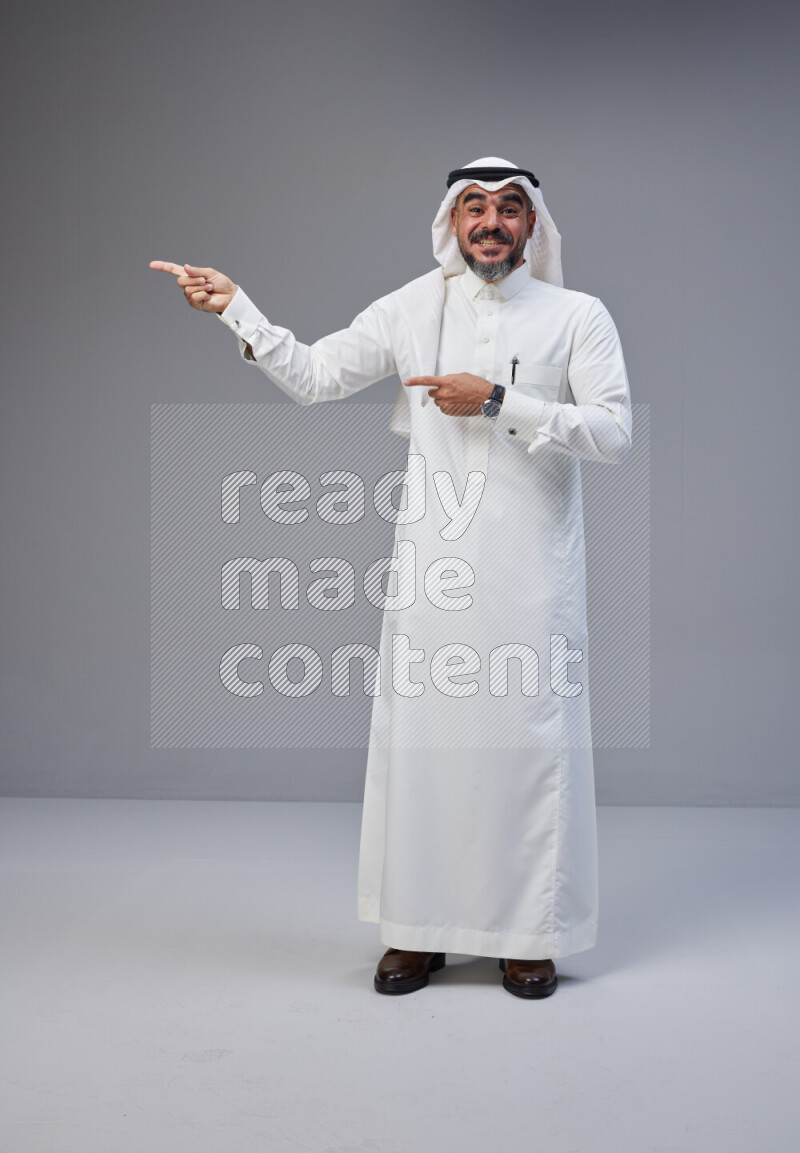 Saudi man Wearing Thob and white Shomag standing interacting with the camera on Gray background