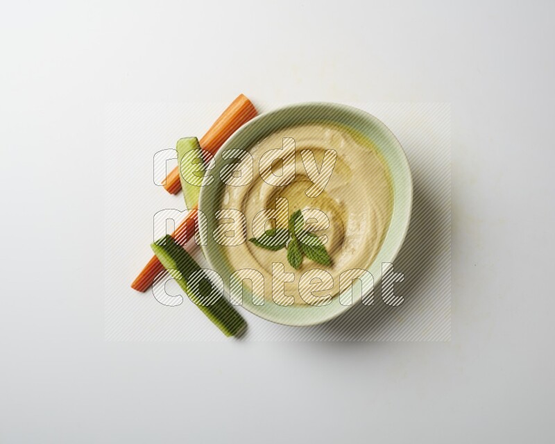 Hummus in a green plate garnished with mint on a white background