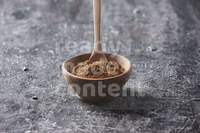Wooden bowl full of cinnamon powder with a wooden spoon on a textured black background in different angles