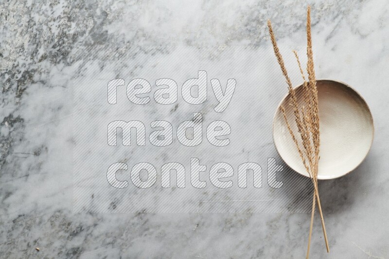 Wheat stalks on beige pottery plate on grey marble background