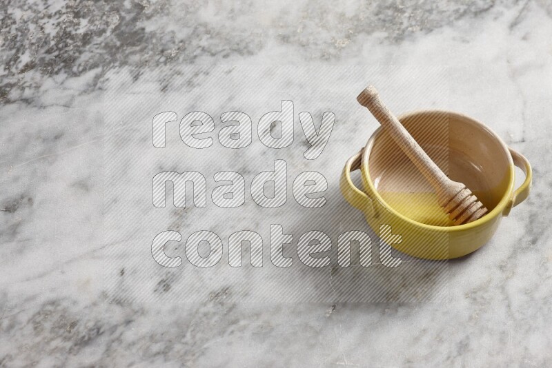 Multicolored pottery bowl with wooden honey dipper in it on grey marble background