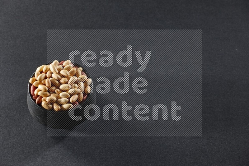 A black pottery bowl full of peeled peanuts on a black background in different angles