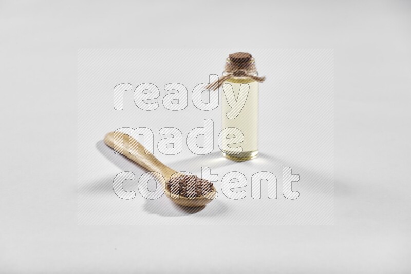 معلقة خشبية مليئة بحبوب بذر الكتان مع زجاجة من زيت بذر الكتان علي خلفية بيضاء