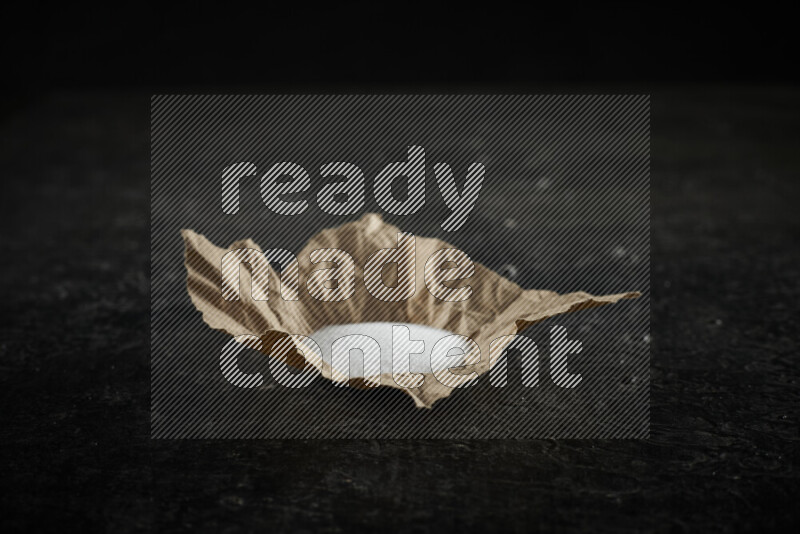 A crumpled piece of paper full of white salt on black background