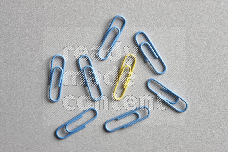 A bunch of blue paper clips with a different colored paper clip in the center on grey background