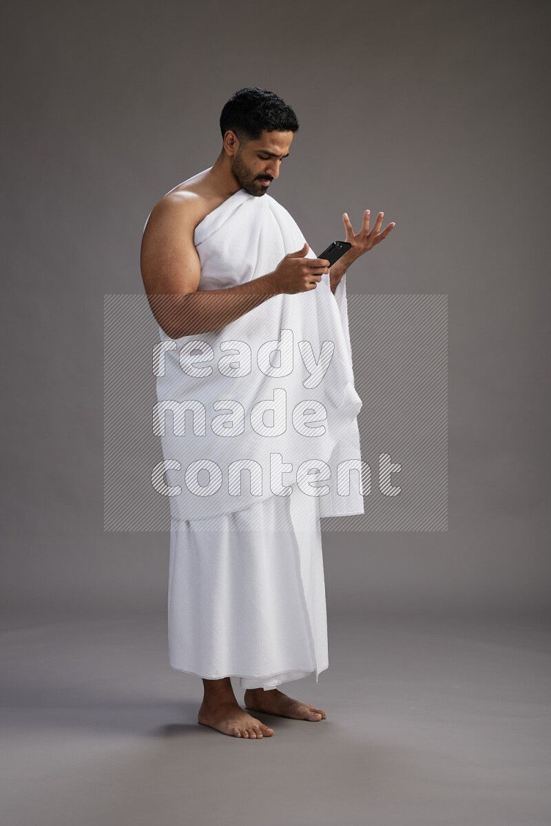 A man wearing Ehram Standing texting on phone on gray background