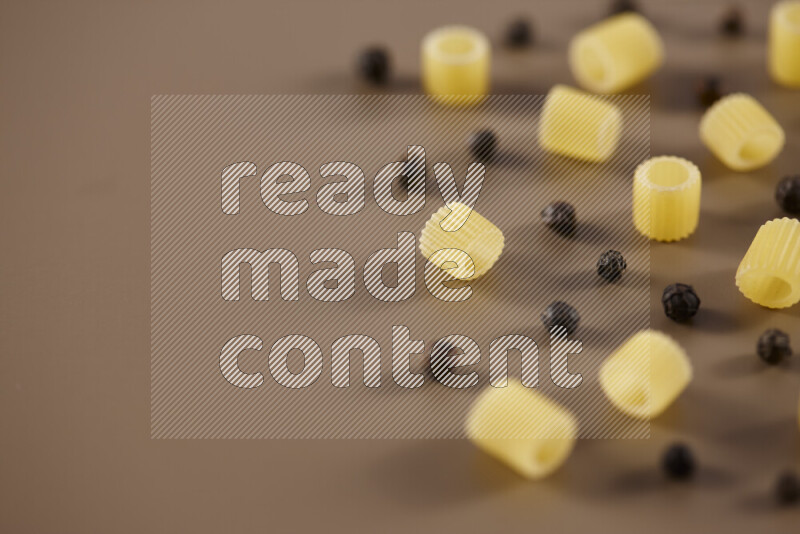 Raw pasta with different ingredients such as cherry tomatoes, garlic, onions, red chilis, black pepper, white pepper, bay laurel leaves, rosemary and cardamom on beige background