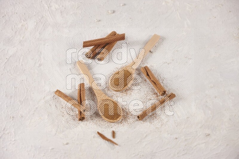 Two wooden spoons full of cinnamon powder with cinnamon sticks on white background