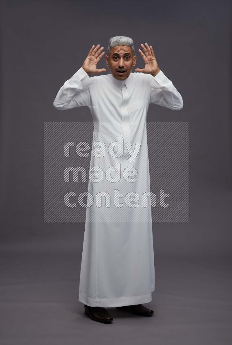 Saudi man wearing thob standing hands behind head on gray background