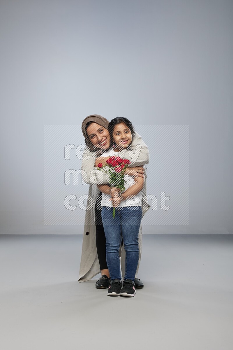 A girl standing giving flowers to her mother on gray background