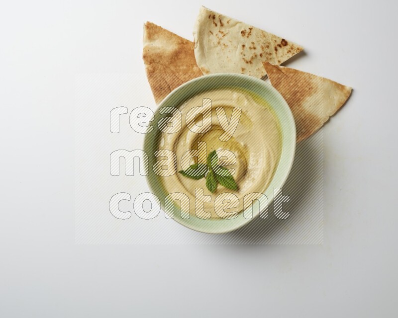 Hummus in a green plate garnished with mint on a white background