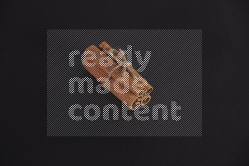 4 Cinnamon sticks stacked and bounded on black flooring