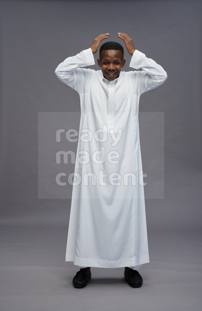Saudi man wearing thob standing hands behind head on gray background