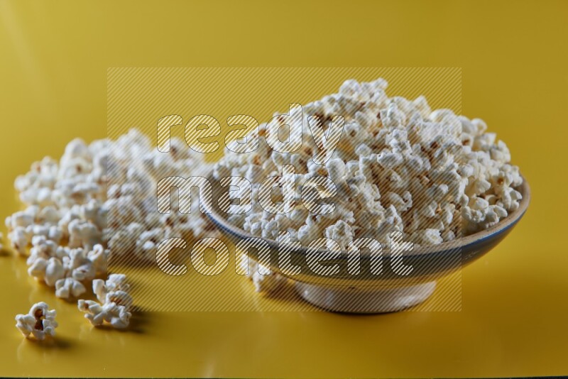 A multicolored ceramic plate full of popcorn with popcorn beside it on a yellow background in different angles