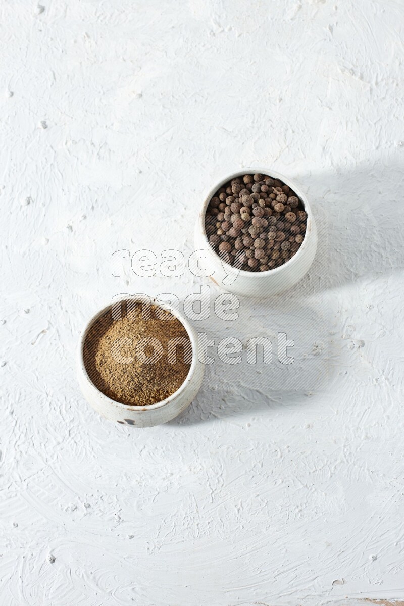 2 beige bowls, one full of allspice powder and the other full of whole balls on a textured white flooring