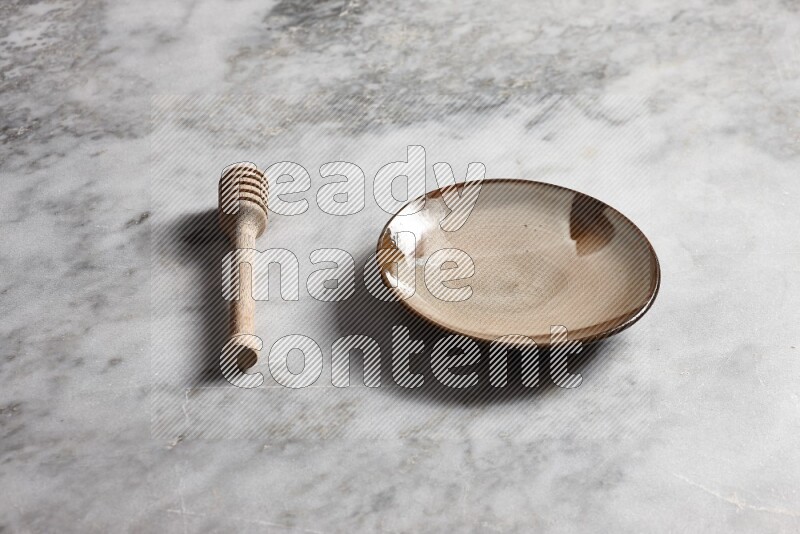 Multicolored pottery plate with wooden honey dipper on the side on grey marble background