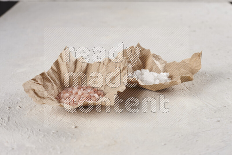 2 crumpled pieces of paper full of pink himalayan salt and white salt on white background