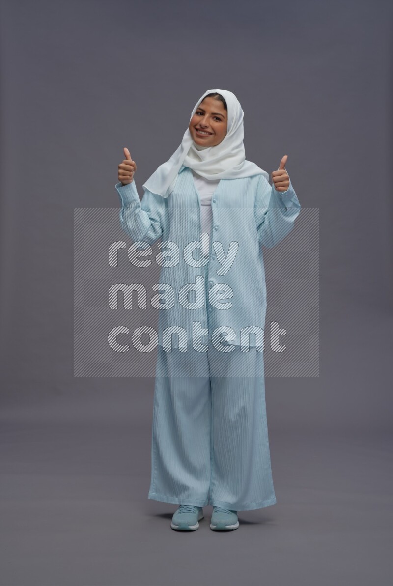 Saudi woman wearing hijab clothes standing interacting with the camera on gray background