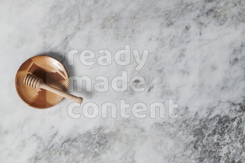 Multicolored pottery plate with wooden honey dipper in it on grey marble background