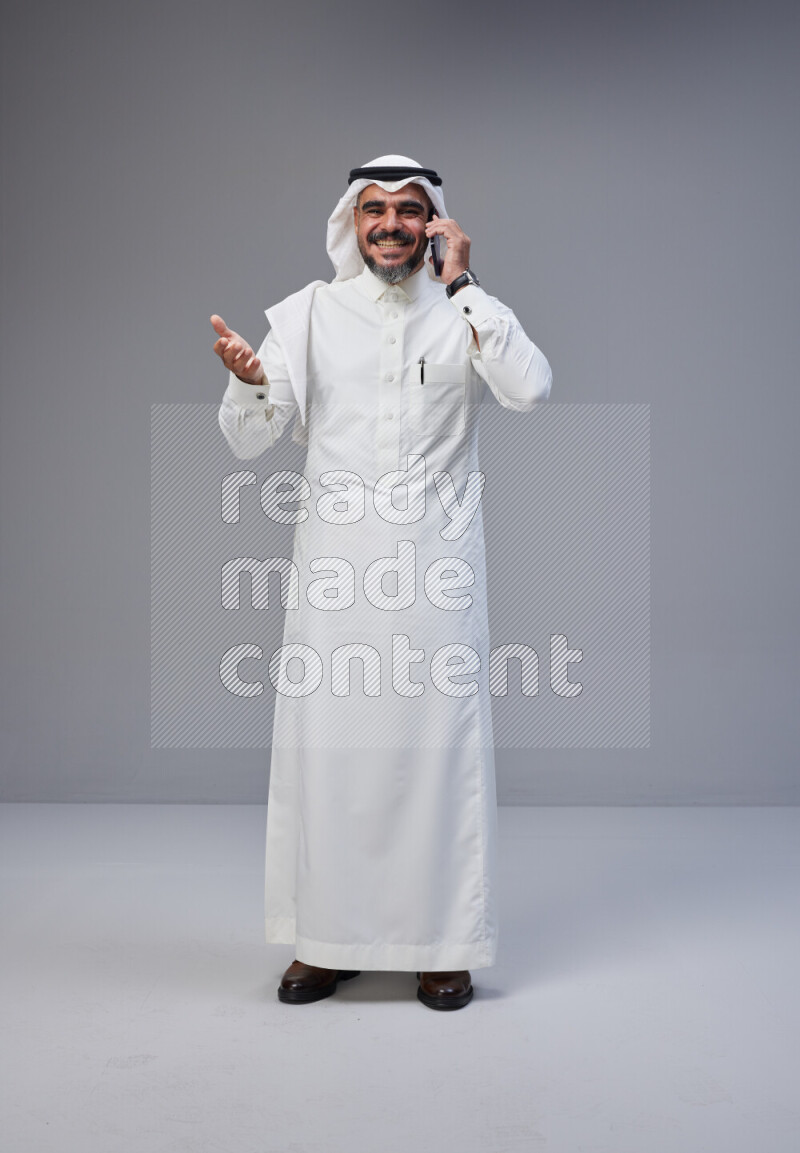 Saudi man Wearing Thob and white Shomag standing talking on phone on Gray background