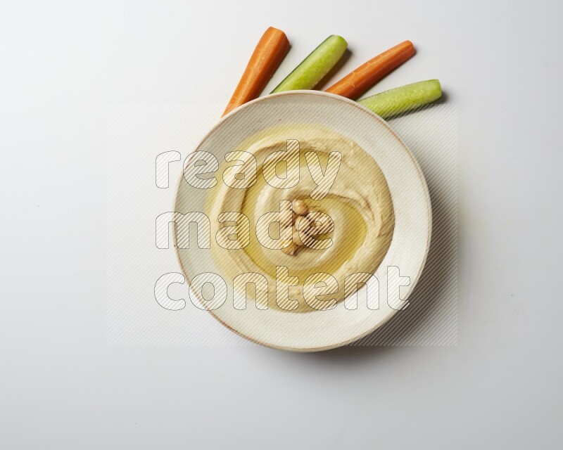 Hummus in a pottry plate garnished with roasted chickpeas on a white background