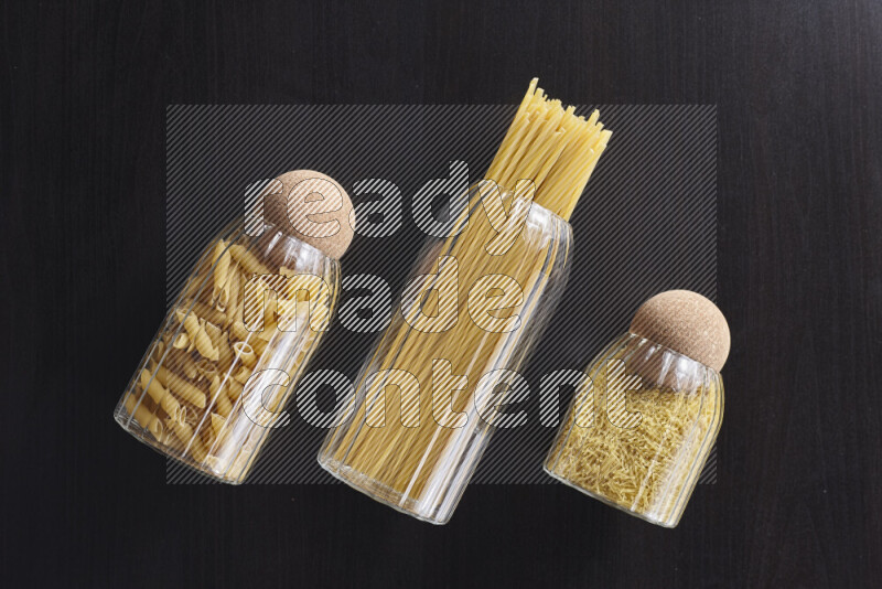 Raw pasta in glass jars on black background