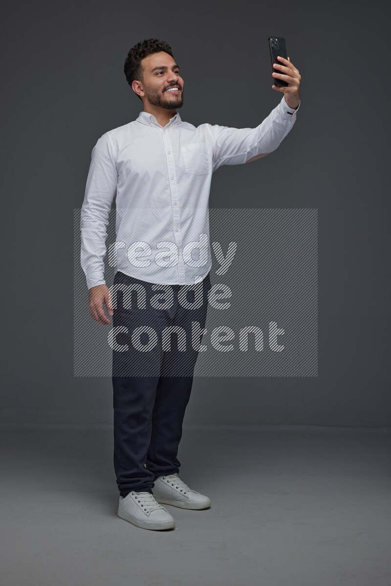 A man wearing smart casual and taking selfie with his phone eye level on a gray background