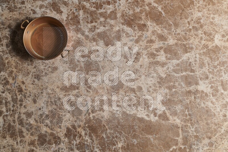 A small copper pan on beige marble background