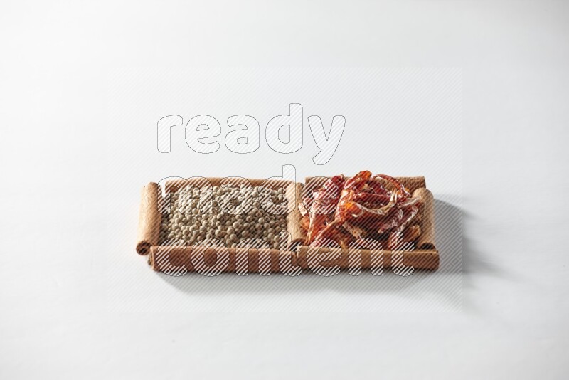 مربعان من أعواد القرفة ممتلئان بالفلفل الحار المجفف وحبوب الفلفل الأبيض علي خلفية بيضاء