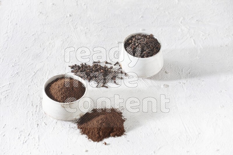 2 Beige ceramic bowls, one full of cloves and the other full of powder on textured white flooring