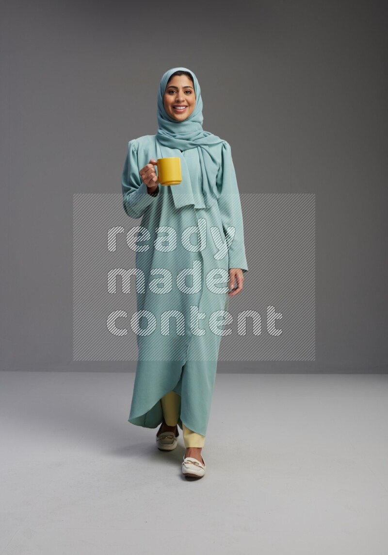 Saudi Woman wearing Abaya standing  holding a mug on Gray background