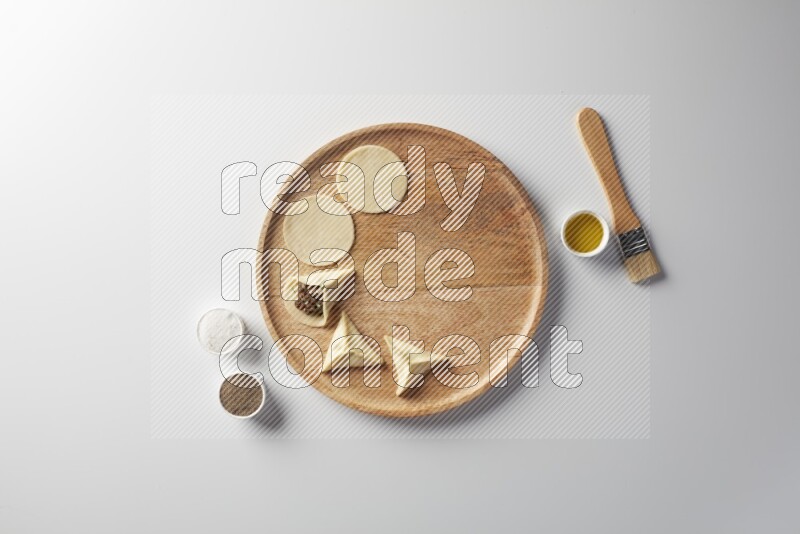 two closed sambosas and one open sambosa filled with meat while salt, black pepper and oil with oil brush aside in a wooden dish on a white background