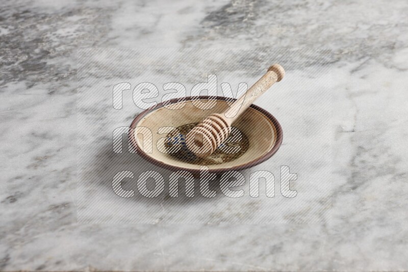Decorative pottery plate with wooden honey dipper in it on grey marble background