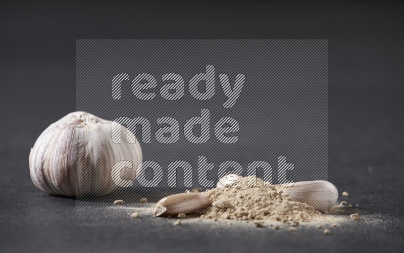 كومة صغيرة من بودرة الثوم مع بعض فصوص الثوم ورأس ثوم كاملة على خلفية سوداء