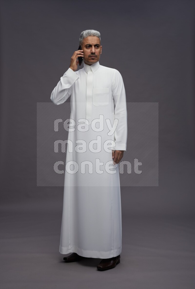 Saudi man wearing thob standing talking on phone on gray background