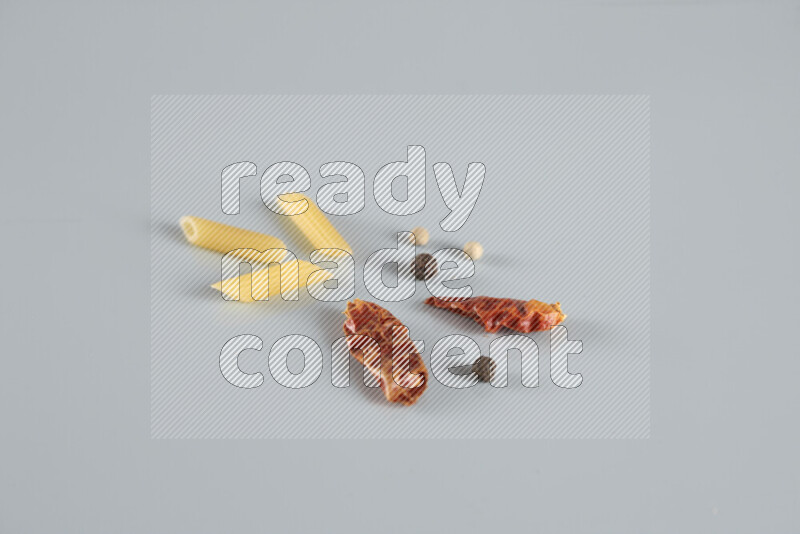 Raw pasta with different ingredients such as cherry tomatoes, garlic, onions, red chilis, black pepper, white pepper, bay laurel leaves, rosemary, cardamom and mushrooms on light blue background