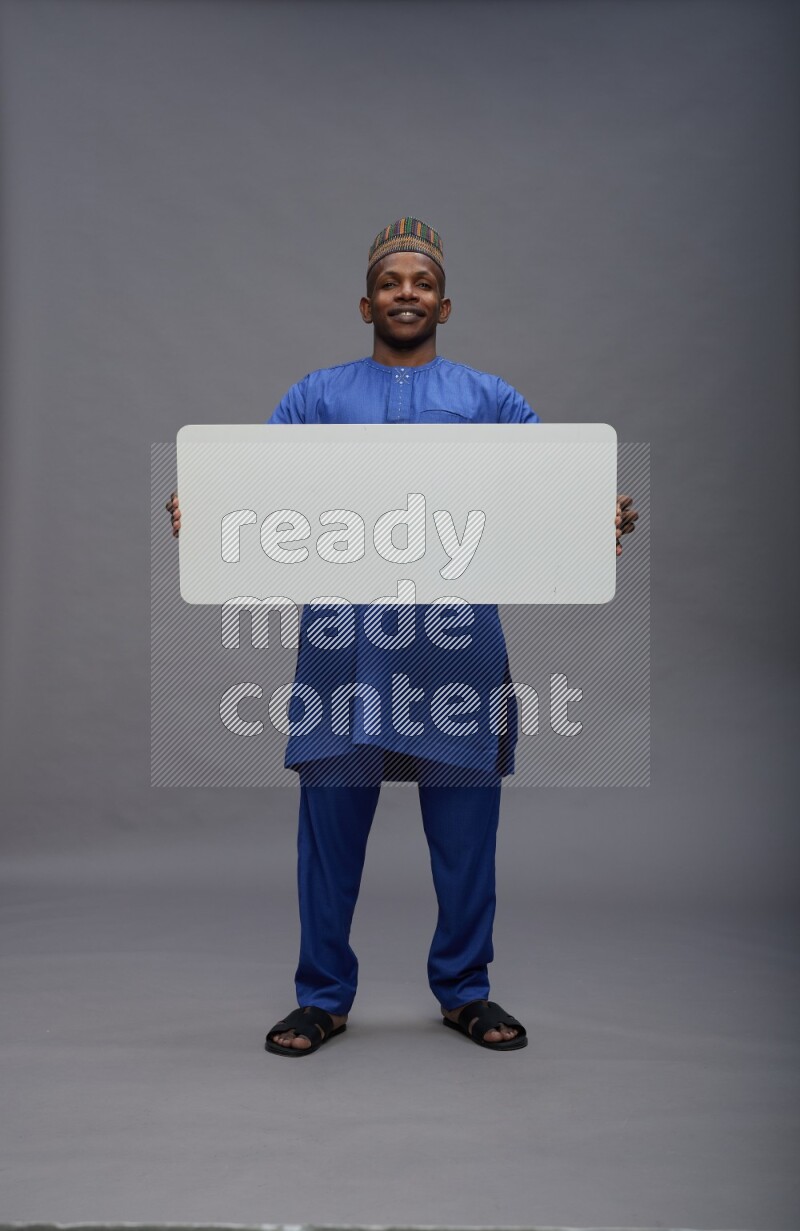 Man wearing Nigerian outfit standing holding board on gray background