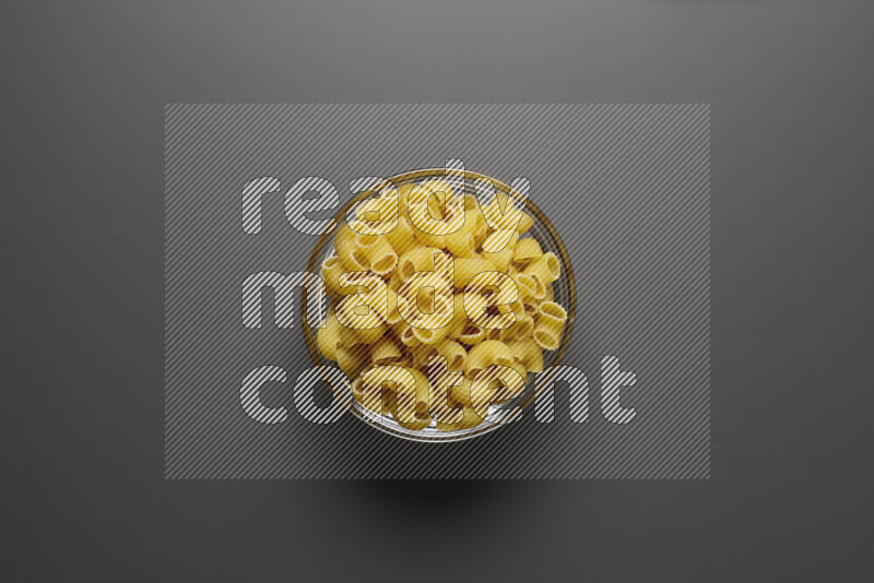 Elbow pasta in a glass bowl on grey background