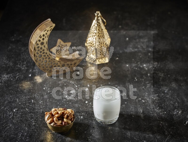 Nuts in a metal bowl with sobia beside golden lanterns in a dark setup