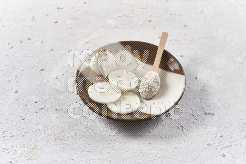 A wooden spoon full of onion powder with sliced onions, all on a pottery plate on white background