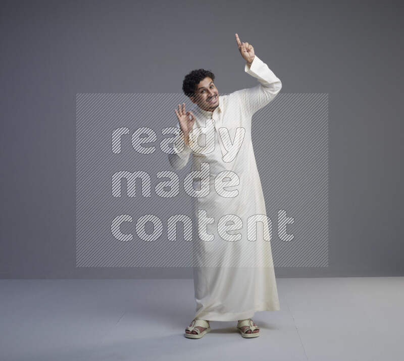 A Saudi man standing wearing thob interacting with the camera on gray background