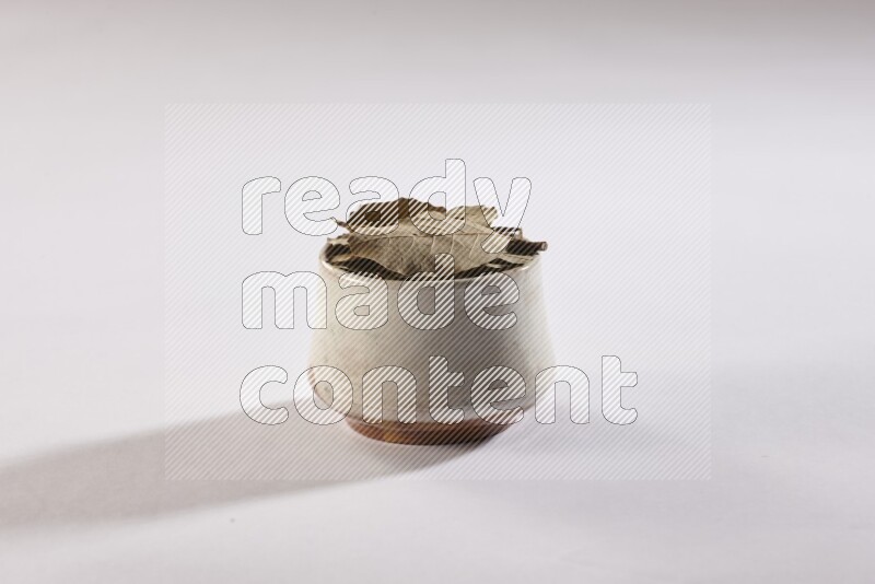 A beige pottery bowl full of dried bay leaves on white flooring
