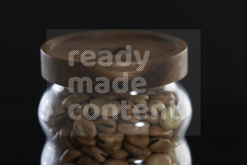 Fava beans in a glass jar on black background