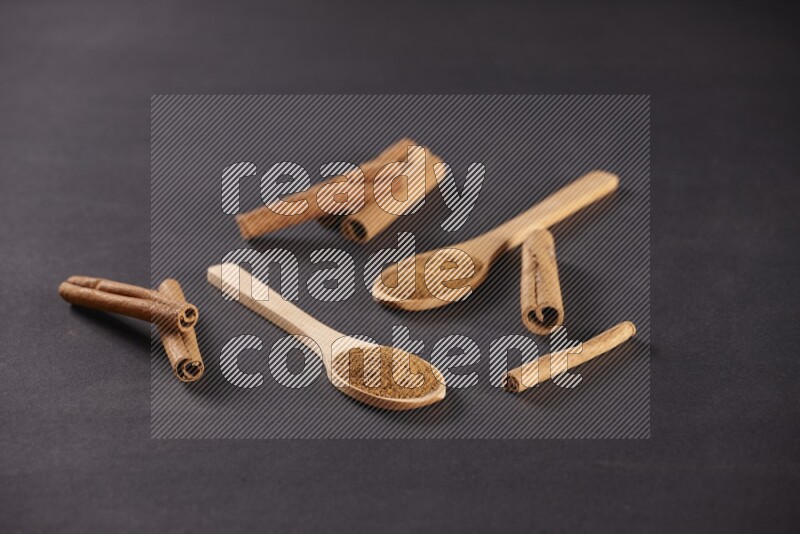 Two wooden spoons full of cinnamon powder with cinnamon sticks on black background